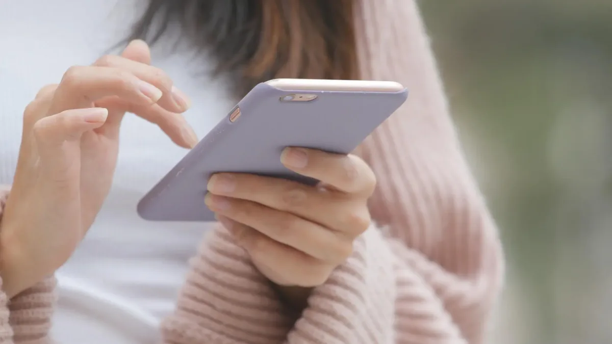 A person holding a smartphone in a lavender case and using its screen