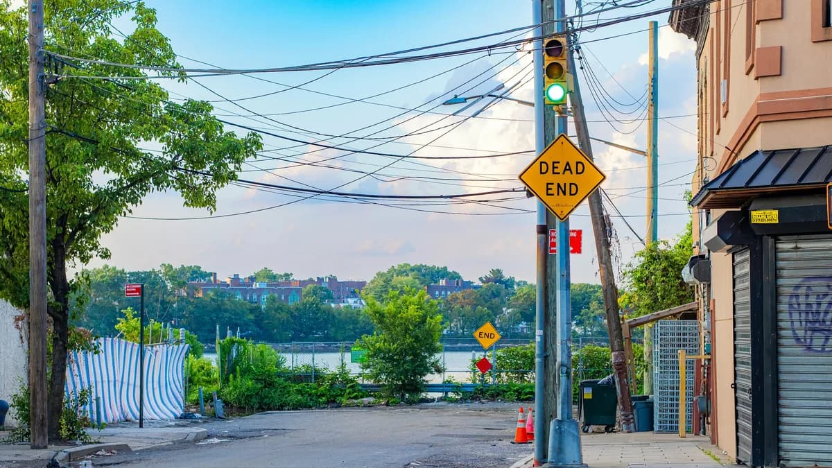 A yellow DEAD END sign at a city street corner, with the road stopping at the water