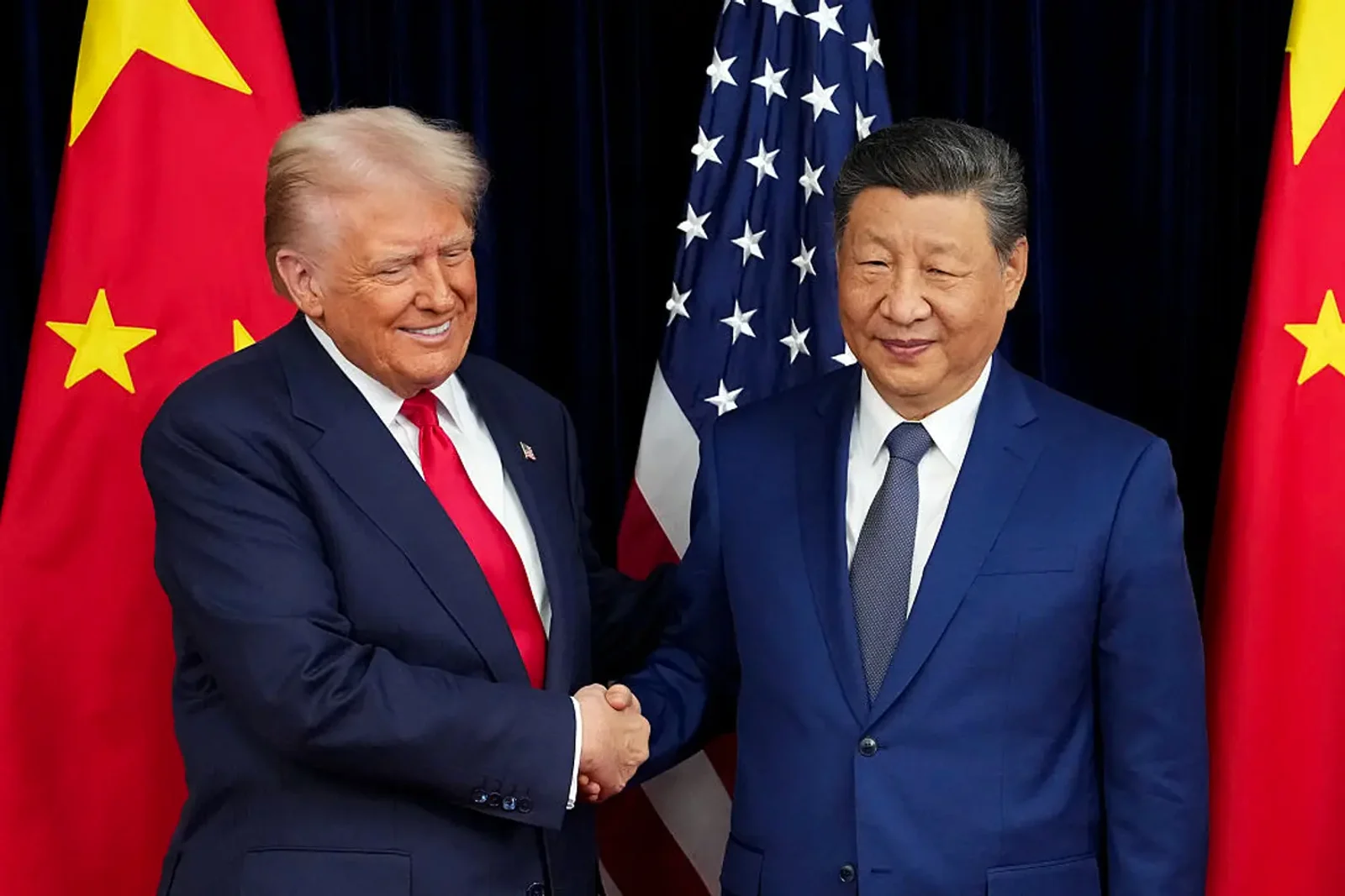 Donald Trump and Xi Jinping shaking hands between United States and China flags for an AntiMedia news article about AI trade and supply chains